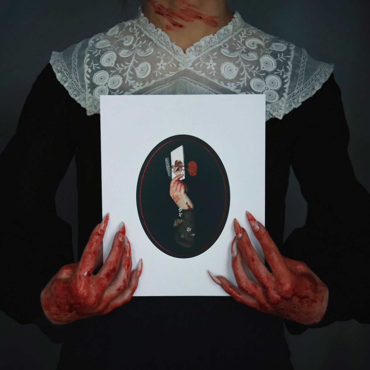 Bloody woman in a Victorian dress with long fingernails holds a gothic collage art print featuring a bloody hand with a razor, a note, and an eye.